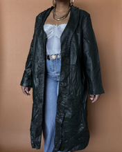 Load image into Gallery viewer, Person wearing a long black coat over a white top and blue jeans on a brown background